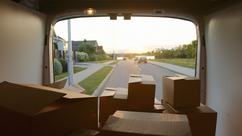 A close-up view of a vehicle's open rear cargo area filled with multiple cardboard boxes of various sizes, some labeled with 'FRAGILE' and 'HANDLE WITH CARE' stickers, indicating careful packing for h